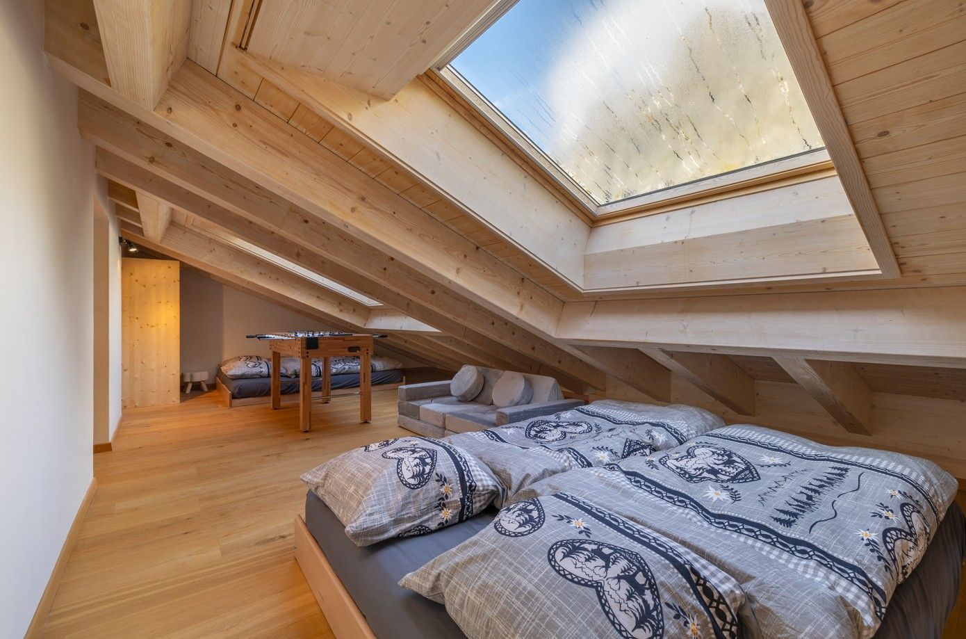 Chambre mansardée avec poutres apparentes, puits de lumière et lit avec linge de lit à motifs.