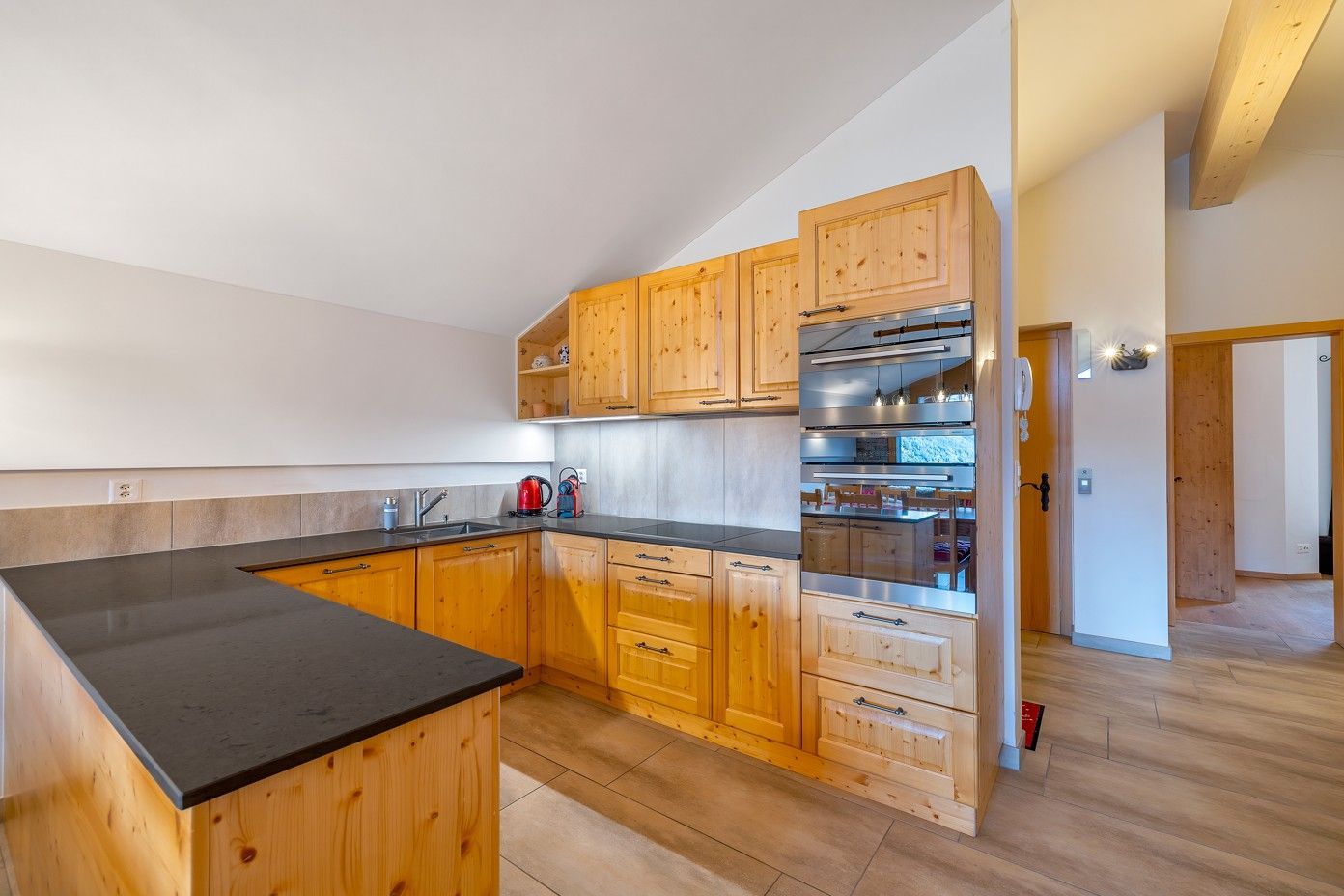 Cuisine en bois avec plan de travail noir et placard intégré à portes vitrées. Intérieur lumineux et spacieux.