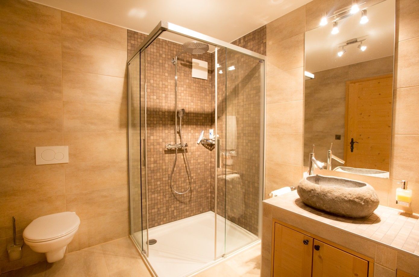 Salle de bains avec douche en verre, lavabo en pierre, toilettes et carrelage beige.