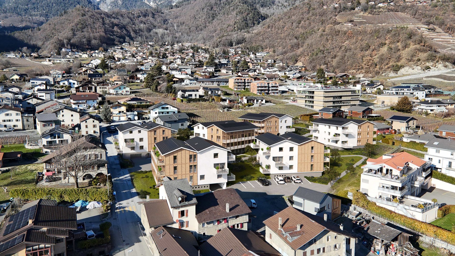 Vue aérienne d'une ville nichée dans une vallée, avec des maisons, des routes et des montagnes brunes en arrière-plan.