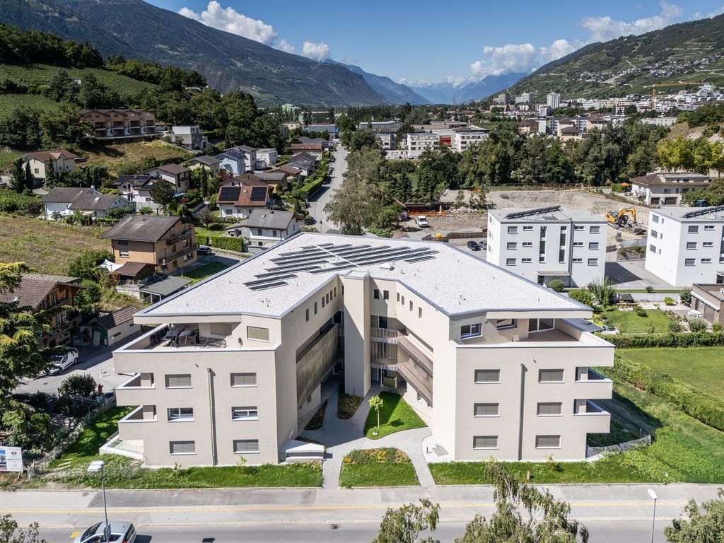 Immeuble moderne à plusieurs étages avec panneaux solaires, quartier résidentiel, montagnes en arrière-plan.