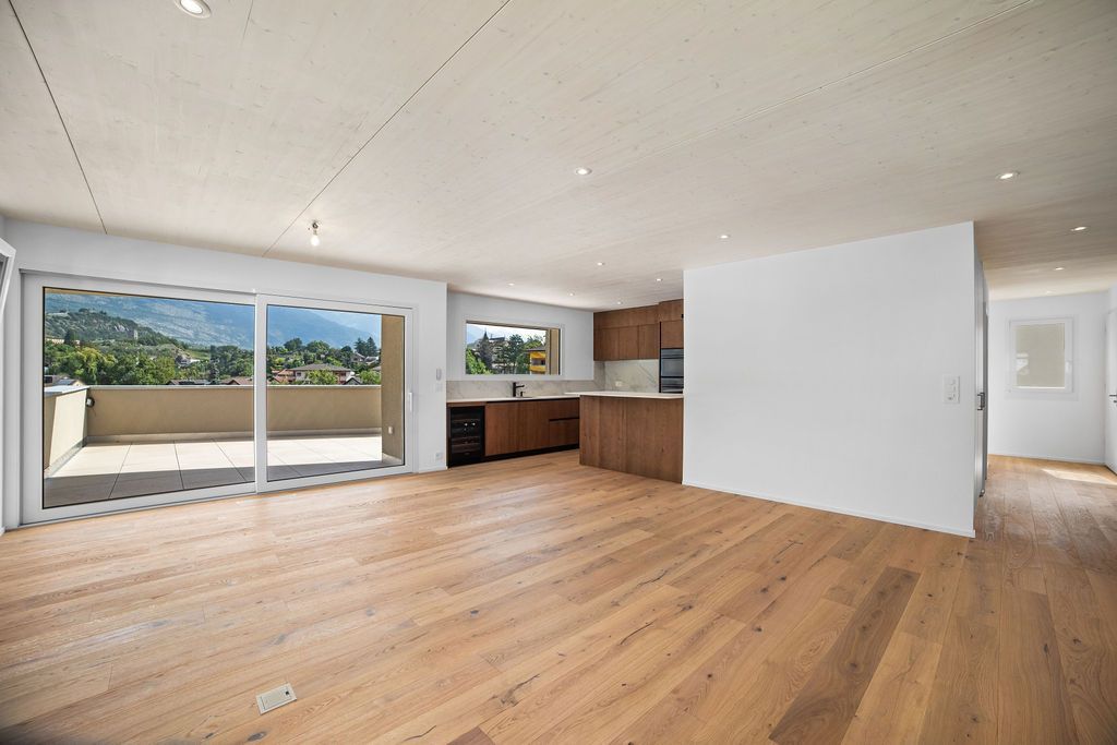 Espace intérieur vide avec parquet, coin cuisine et balcon avec vue sur la montagne.