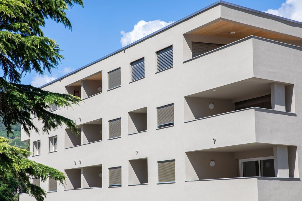 Immeuble moderne aux tons clairs, avec balcons et fenêtres rectangulaires, sous un ciel bleu.