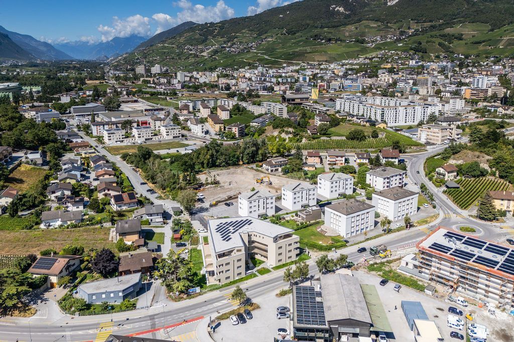 Vue aérienne d'une ville située dans une vallée, avec des bâtiments, des routes et des montagnes en arrière-plan. 