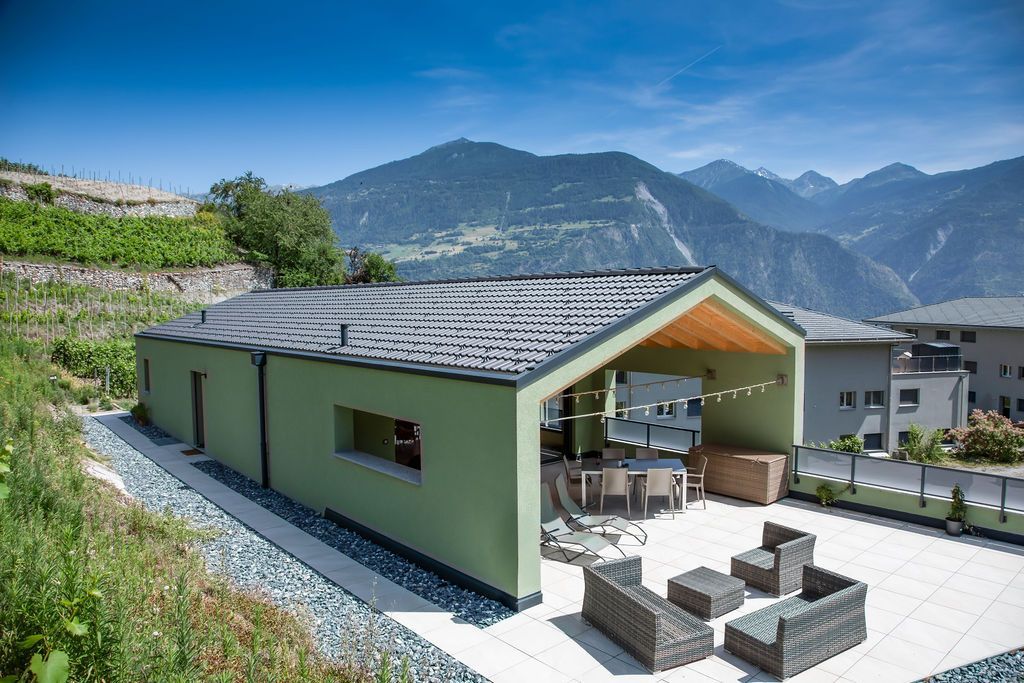 Bâtiment écologique avec terrasse et sièges, donnant sur les montagnes sous un ciel bleu.