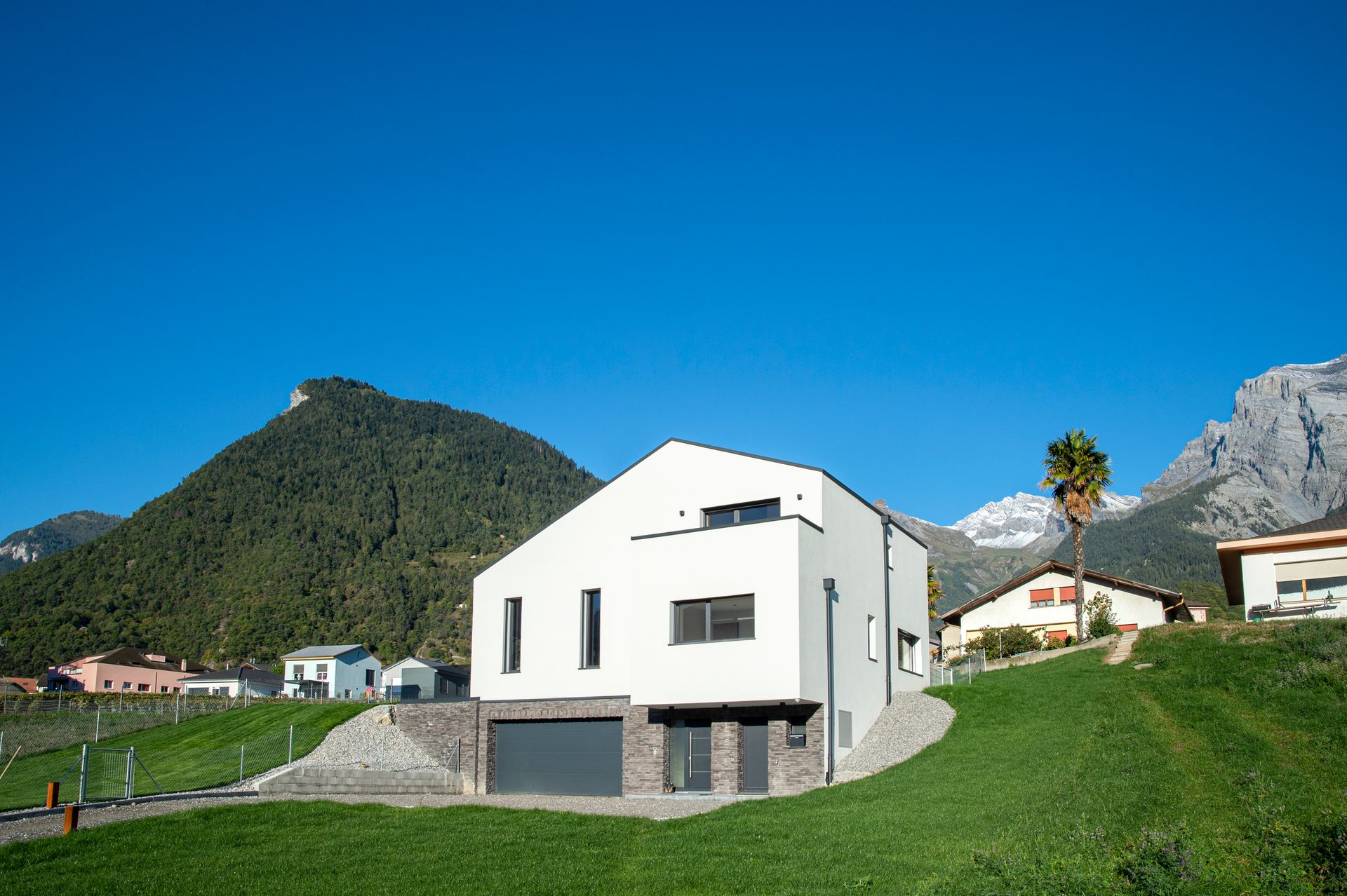Maison moderne blanche avec montagnes en arrière-plan, ciel bleu.