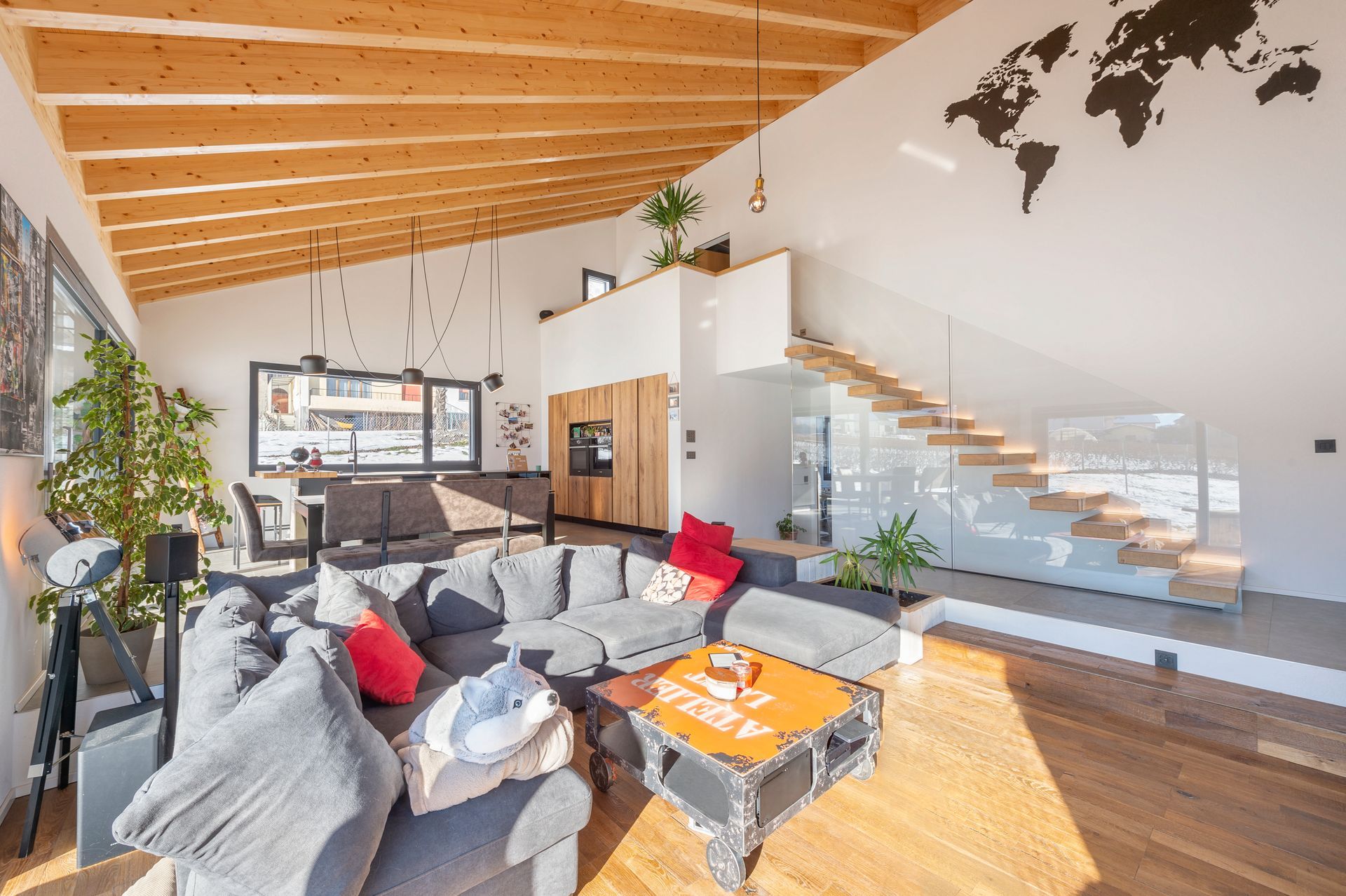 Salon moderne avec plafond en bois, canapé d'angle gris et escalier en bois.