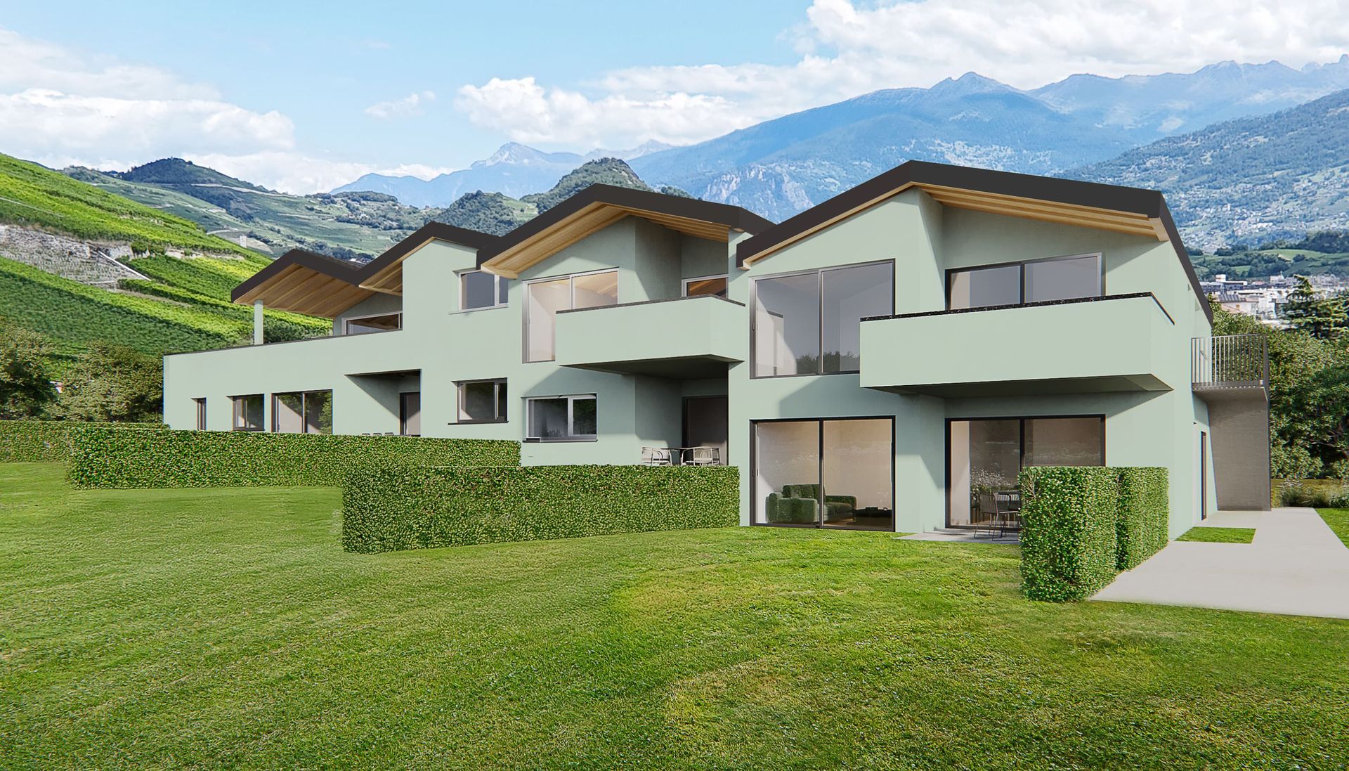 Rangée de maisons de ville vert pâle avec balcons, pelouse luxuriante et montagnes en arrière-plan.