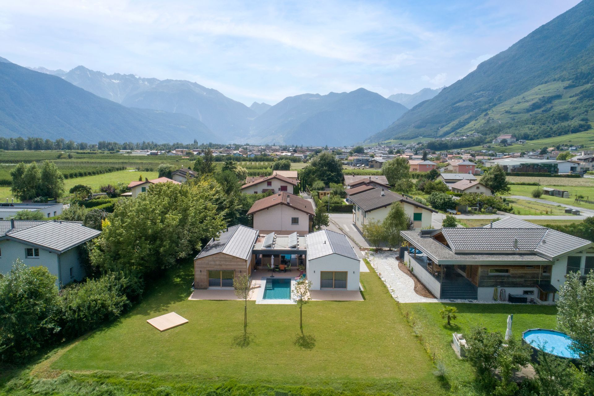 Vue aérienne de maisons modernes avec piscine dans une vallée montagneuse.