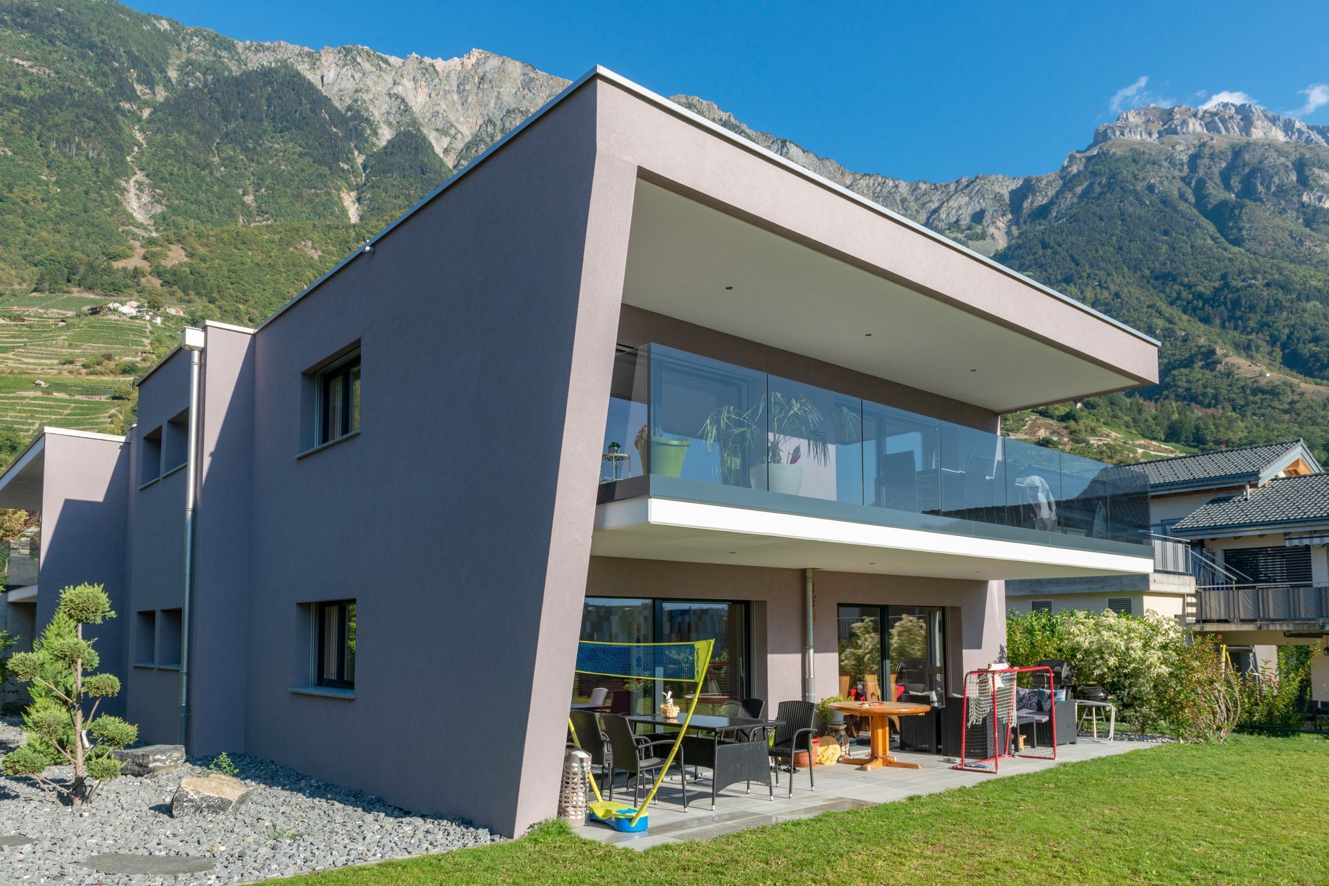 Maison grise moderne avec balcon, balustrade en verre et vue sur les montagnes.