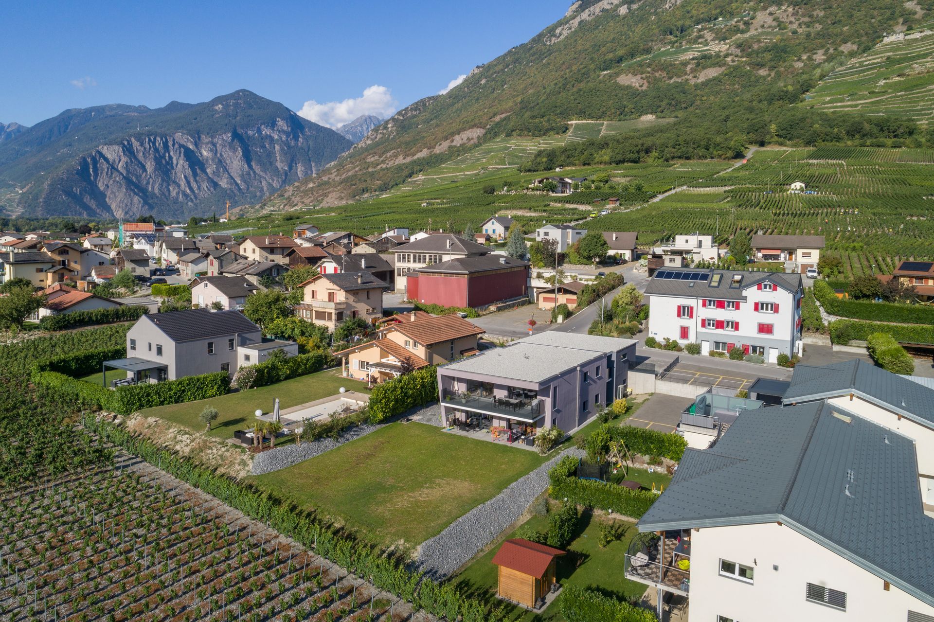 Vue aérienne d'un village niché dans une vallée, avec des vignobles et une montagne en arrière-plan.