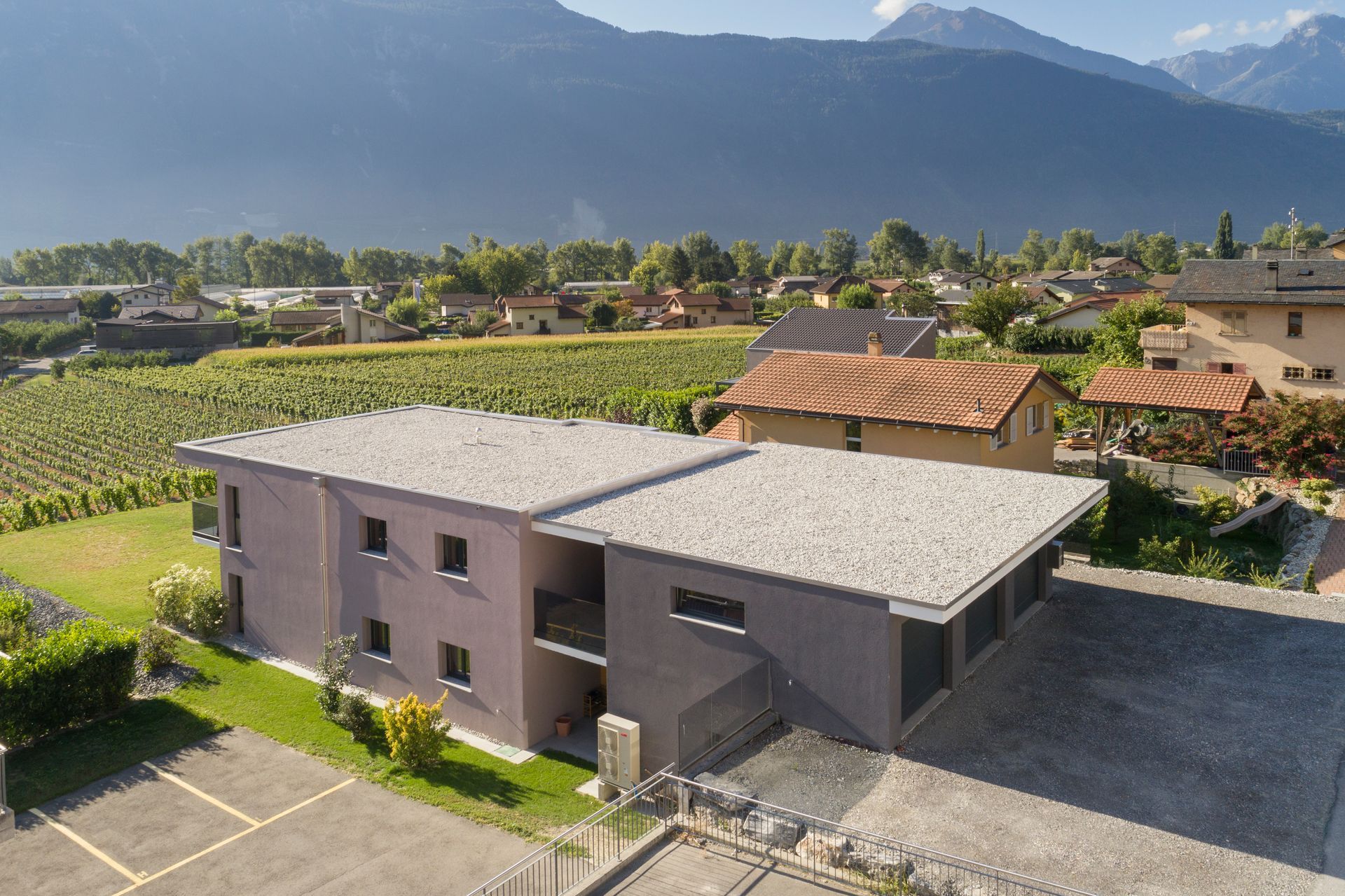 Bâtiment moderne gris à toit plat, situé près des vignobles et des montagnes.