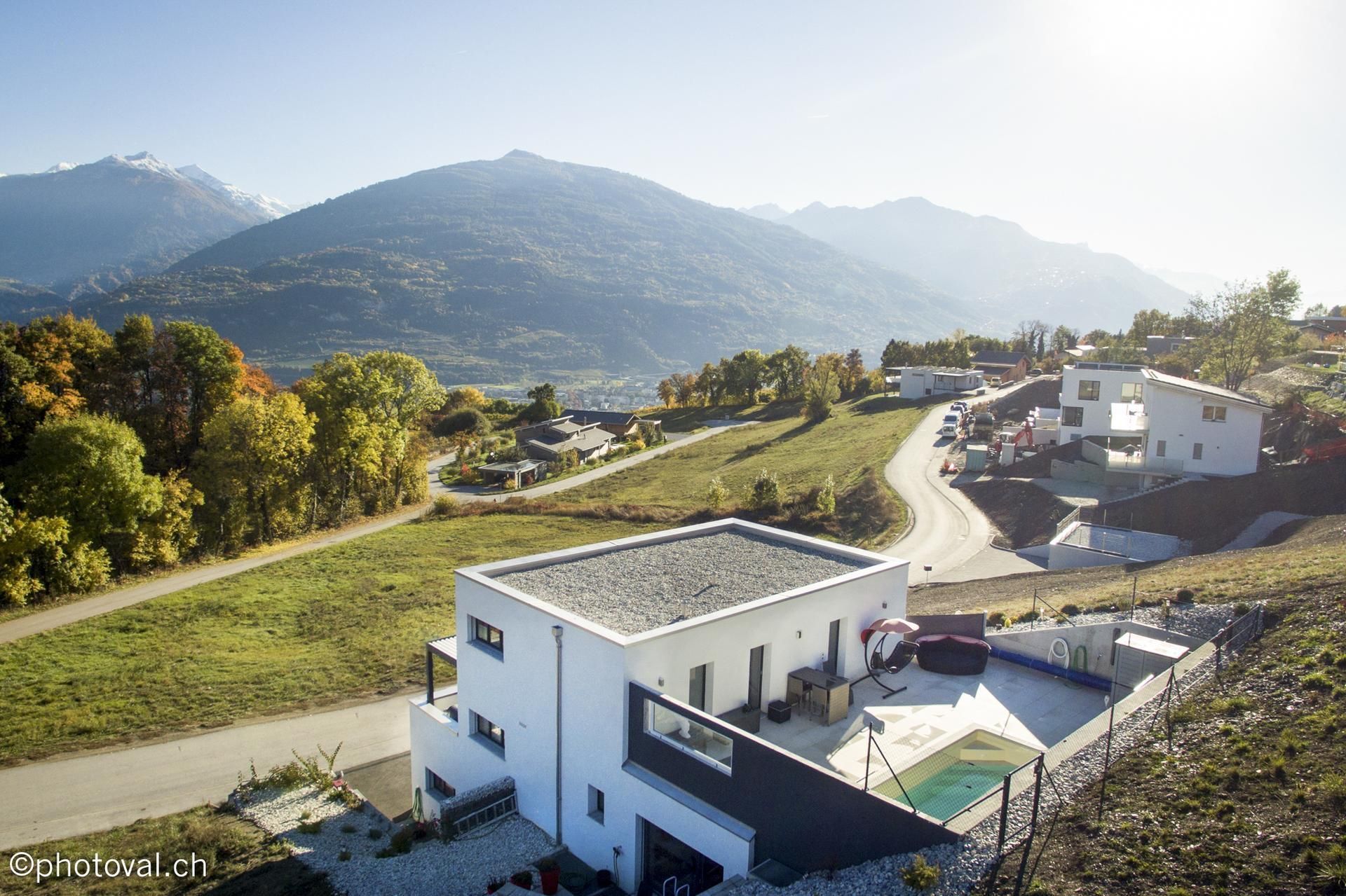 Maisons modernes à flanc de colline avec piscine, surplombant les montagnes et une route sinueuse.