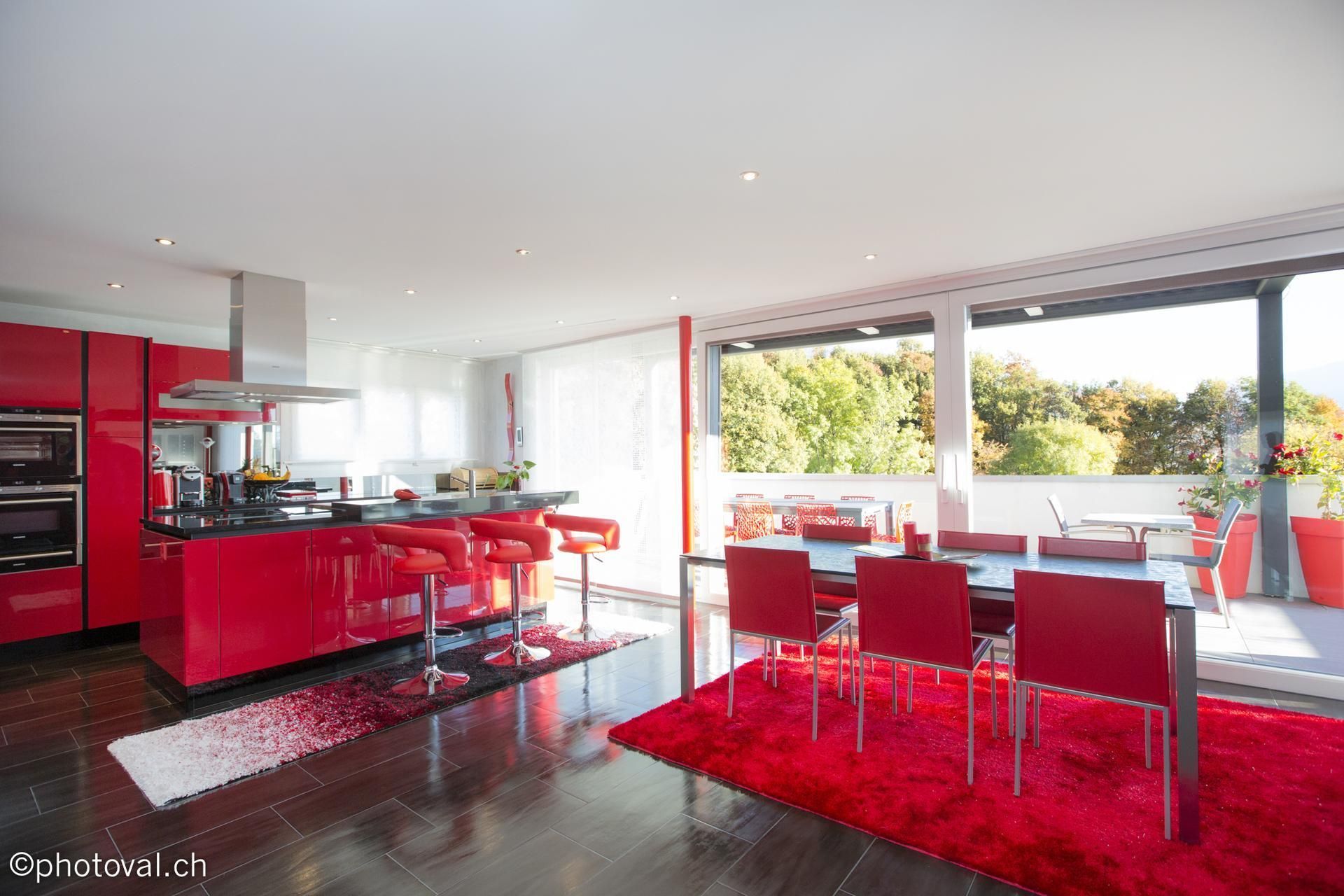 Cuisine et salle à manger modernes rouges avec balcon donnant sur les arbres.