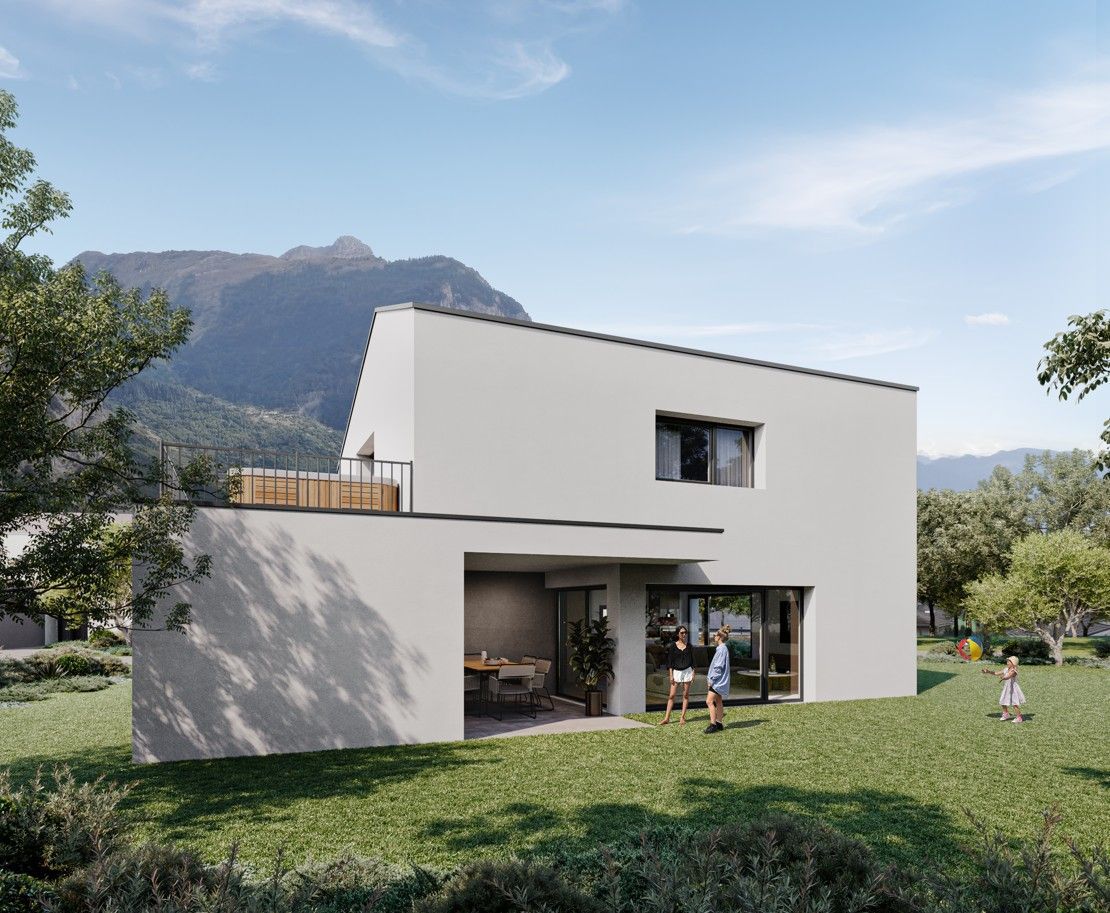 Maison blanche moderne à toit plat, patio ouvert et jardin gazonné, avec les montagnes en toile de fond. Des personnes se trouvent dans le jardin.