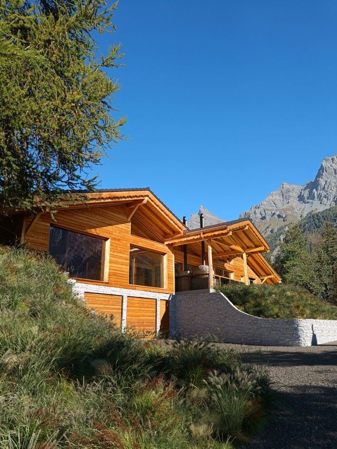 Cabane en bois avec les montagnes en arrière-plan, un escalier et un ciel bleu dégagé.