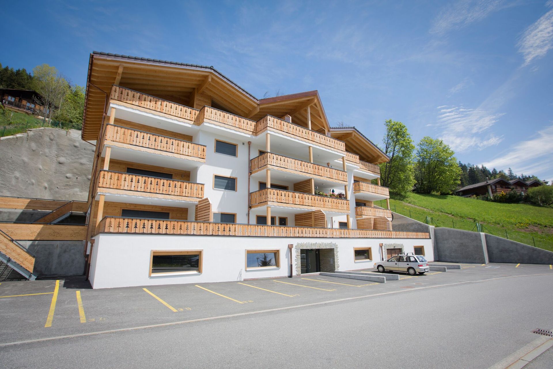 Immeuble moderne à plusieurs étages avec balcons, parking et terrain en pente gazonné.