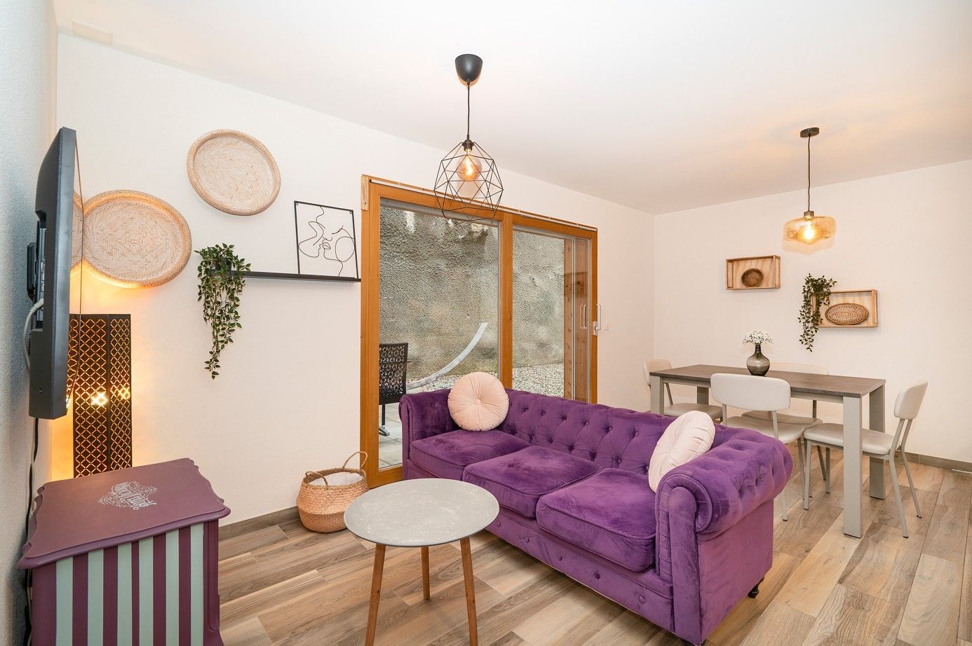 Salon avec canapé violet, table à manger, paniers muraux décoratifs et fenêtre.