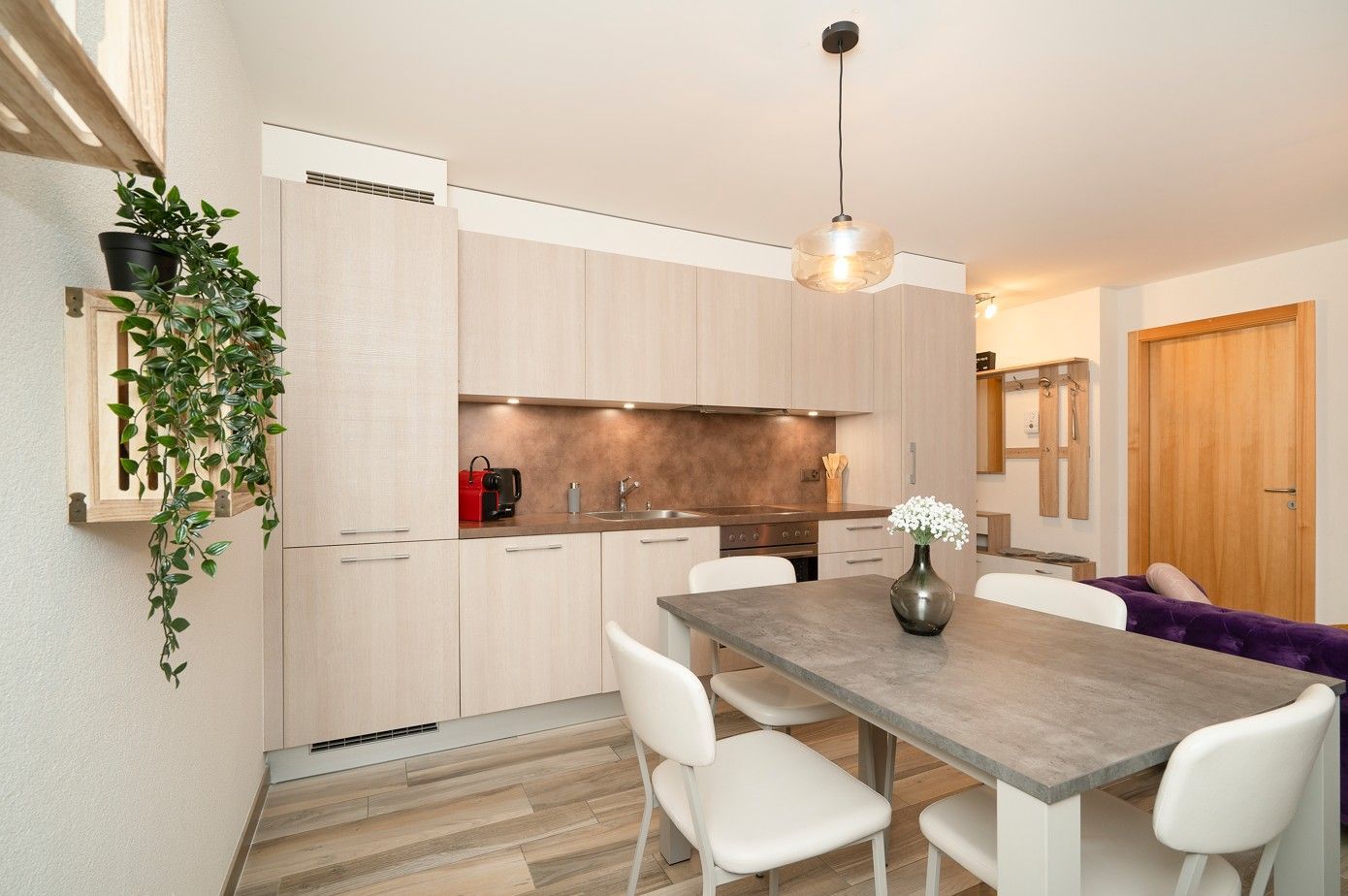 Une cuisine et un coin repas avec des placards en bois clair et une table grise. 