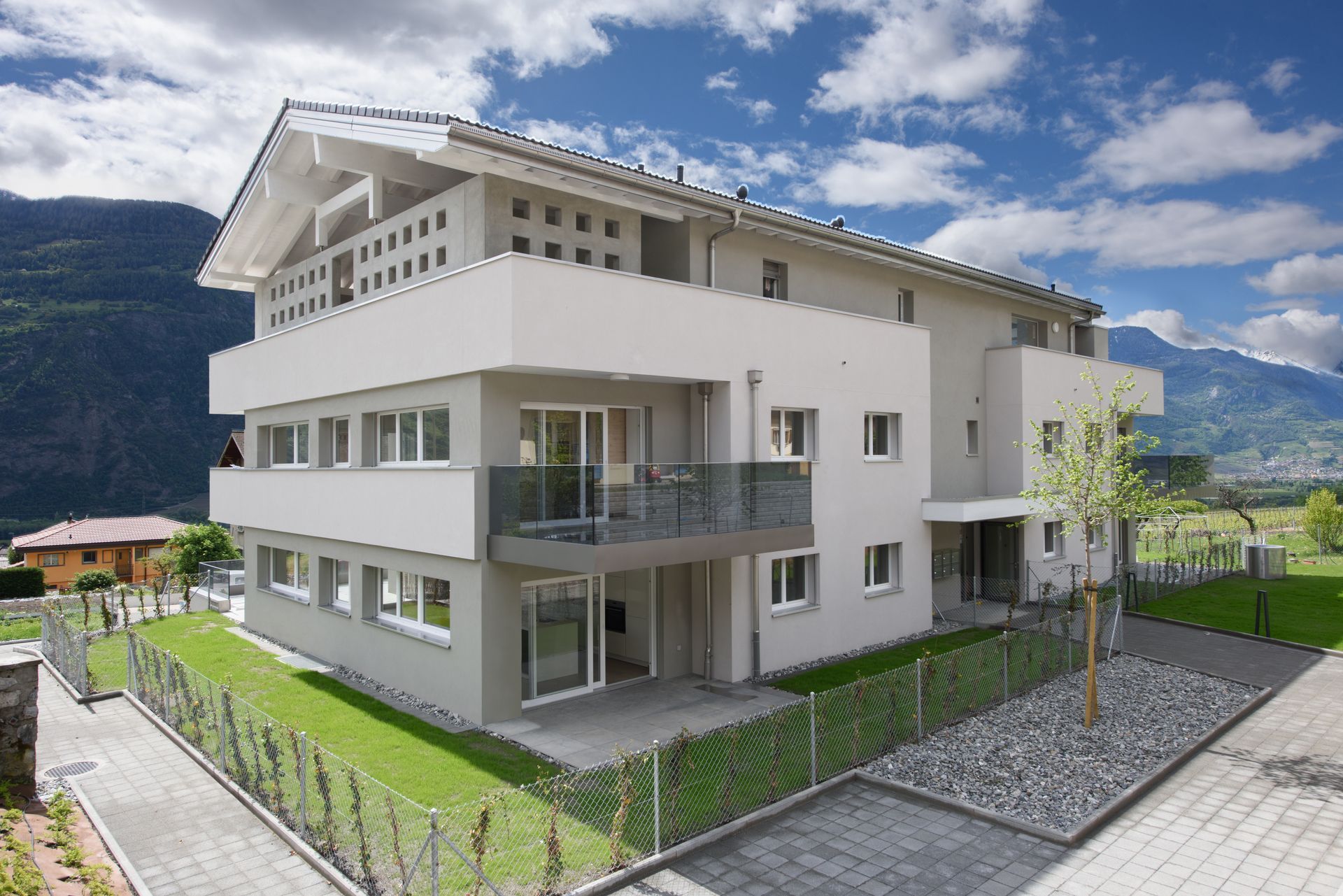 Immeuble d'appartements moderne avec balcons, avec les montagnes en toile de fond sous un ciel partiellement nuageux.