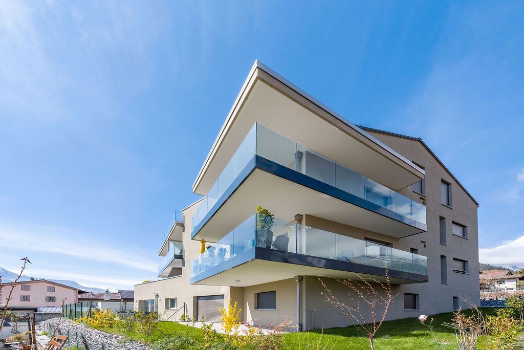 Immeuble d'appartements moderne avec balcons vitrés, sous un ciel bleu.