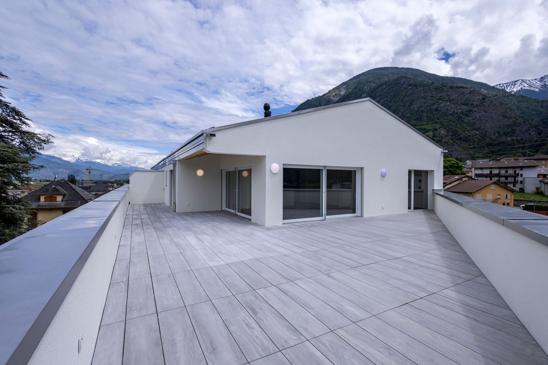 Terrasse blanche sur le toit avec plancher en bois, vue sur le bâtiment et les montagnes.