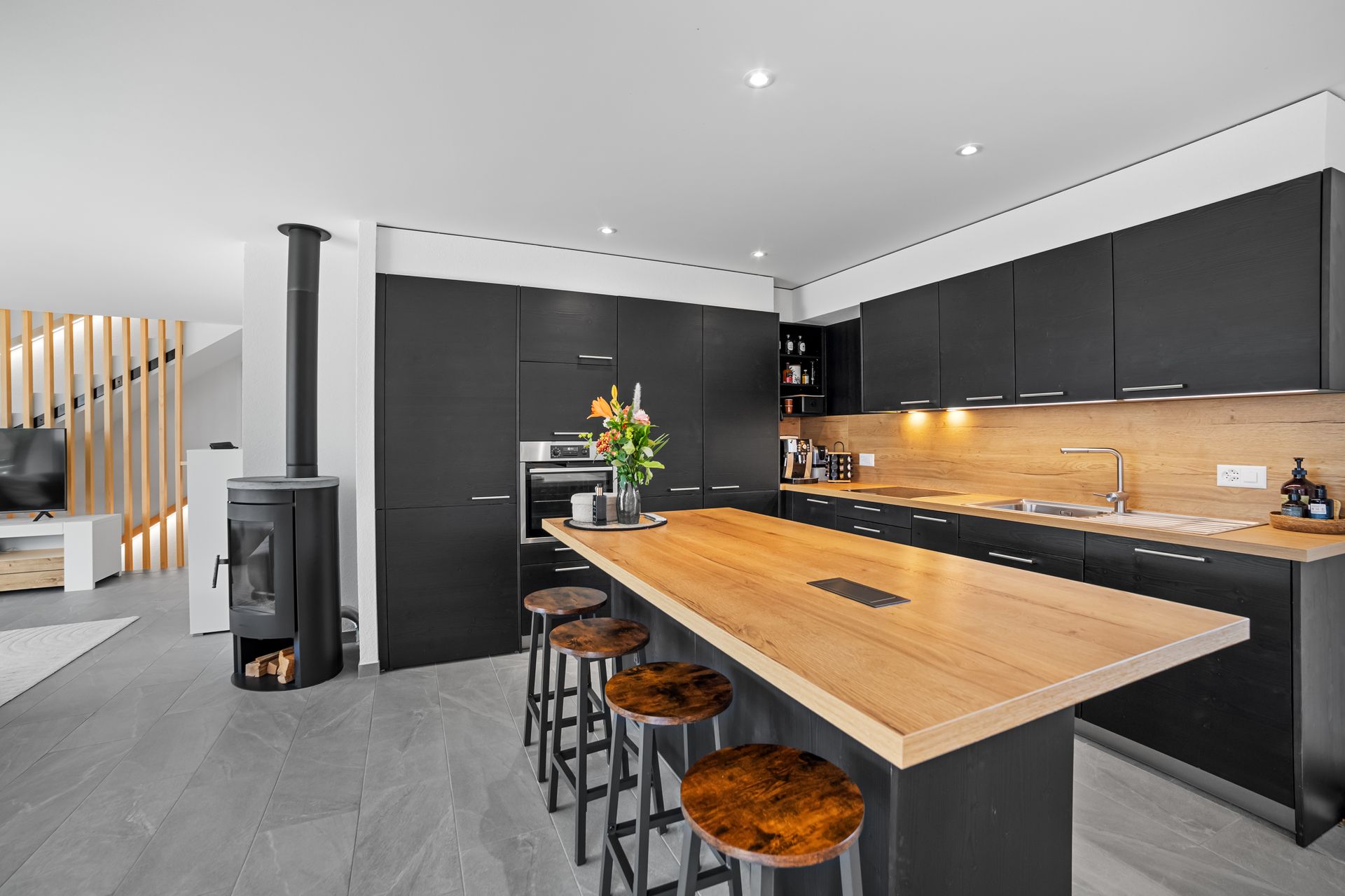 Cuisine moderne avec armoires noires, îlot en bois et poêle à bois.