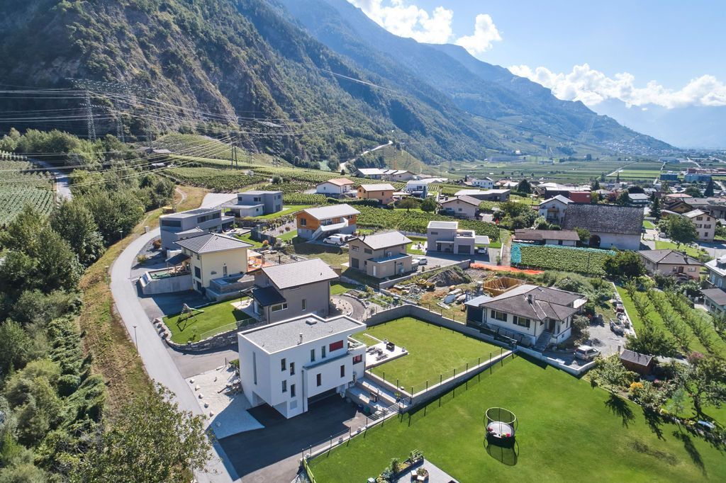 Vue aérienne d'une ville située dans une vallée, avec des maisons, des champs verdoyants, et une route.