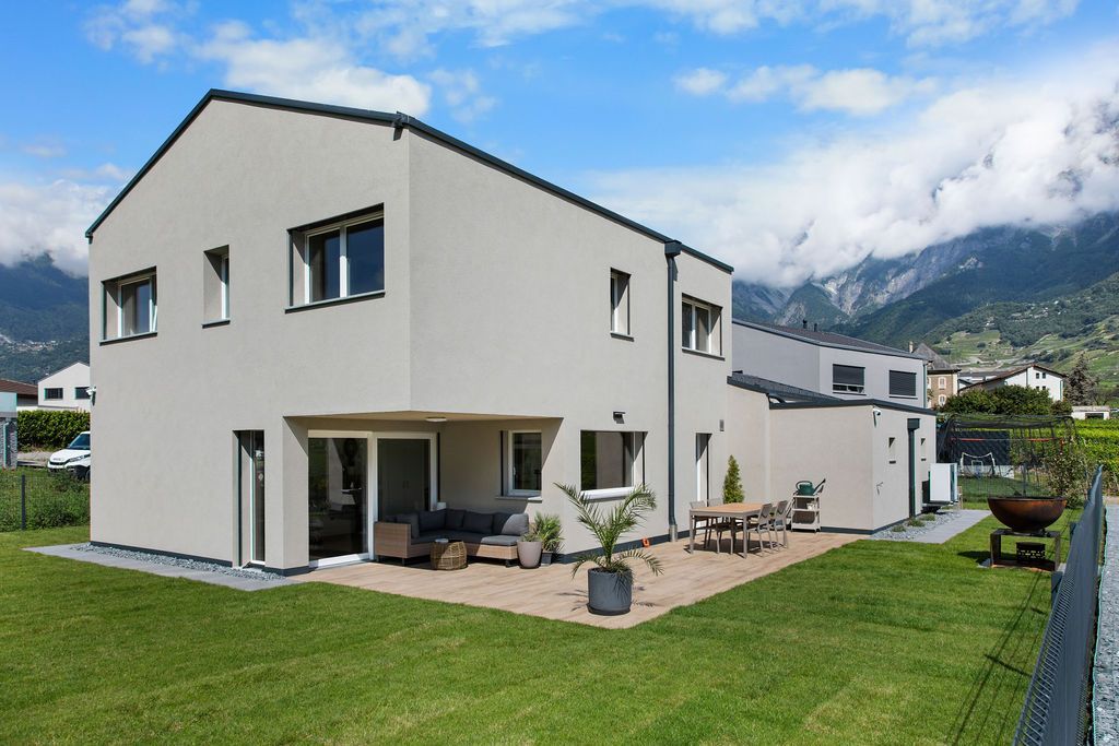 Maison moderne à deux étages avec une façade gris clair, comprenant un patio, un jardin et une vue sur les montagnes.
