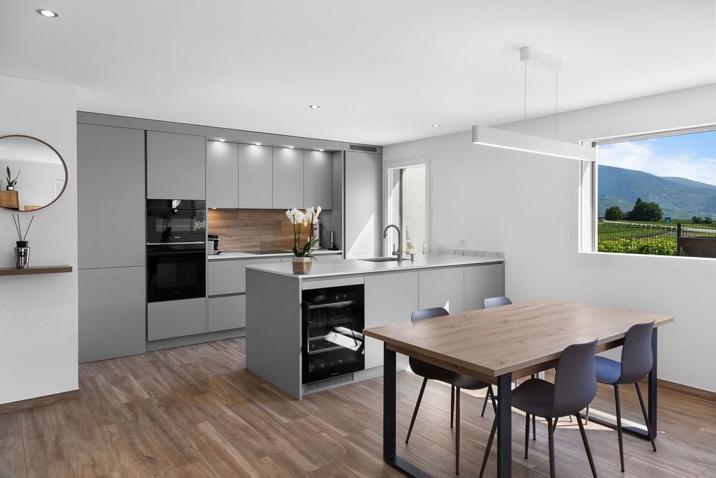 Cuisine moderne avec placards gris, îlot central avec cave à vin, table à manger.