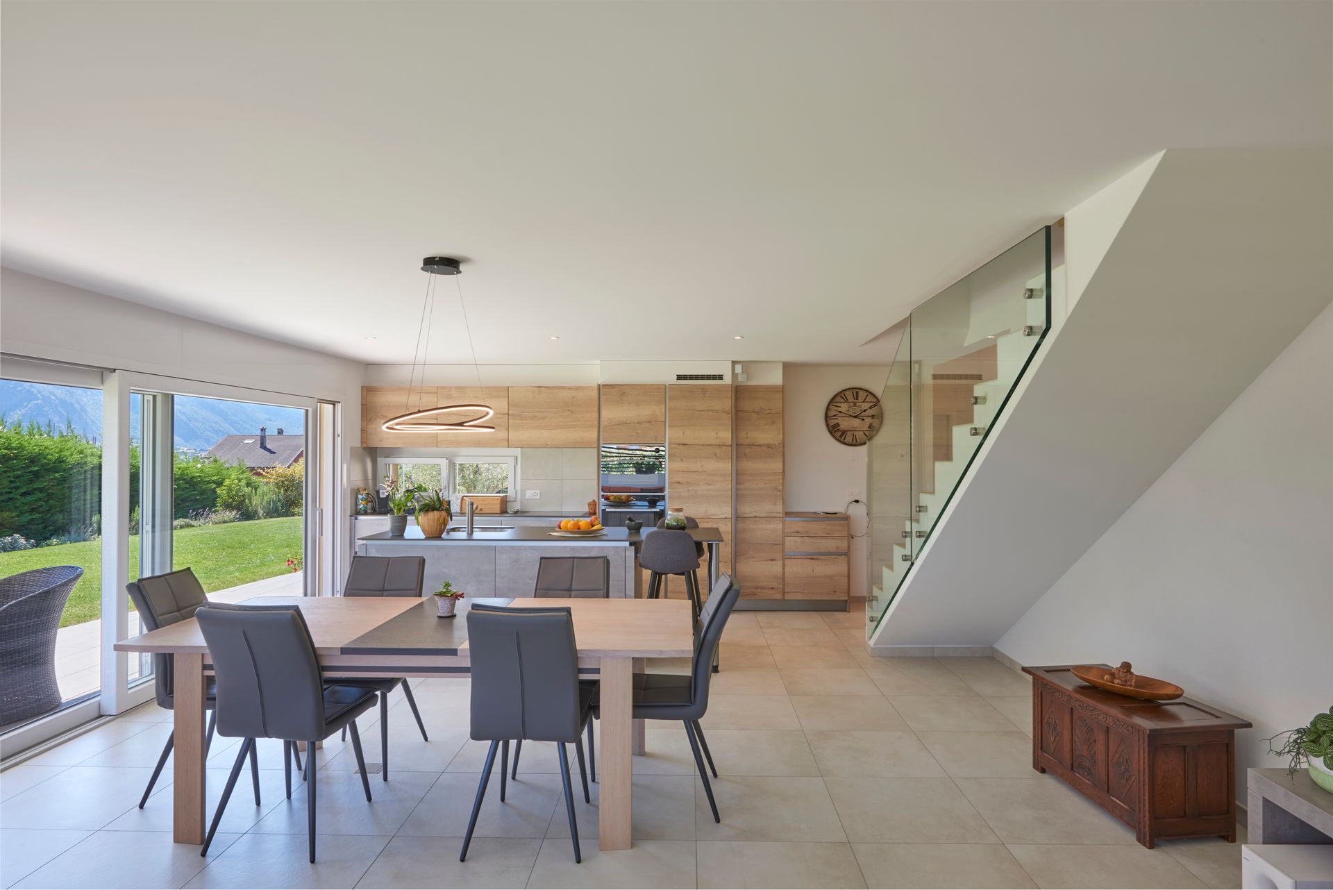Cuisine et salle à manger modernes à aire ouverte avec table en bois, chaises et portes coulissantes en verre.