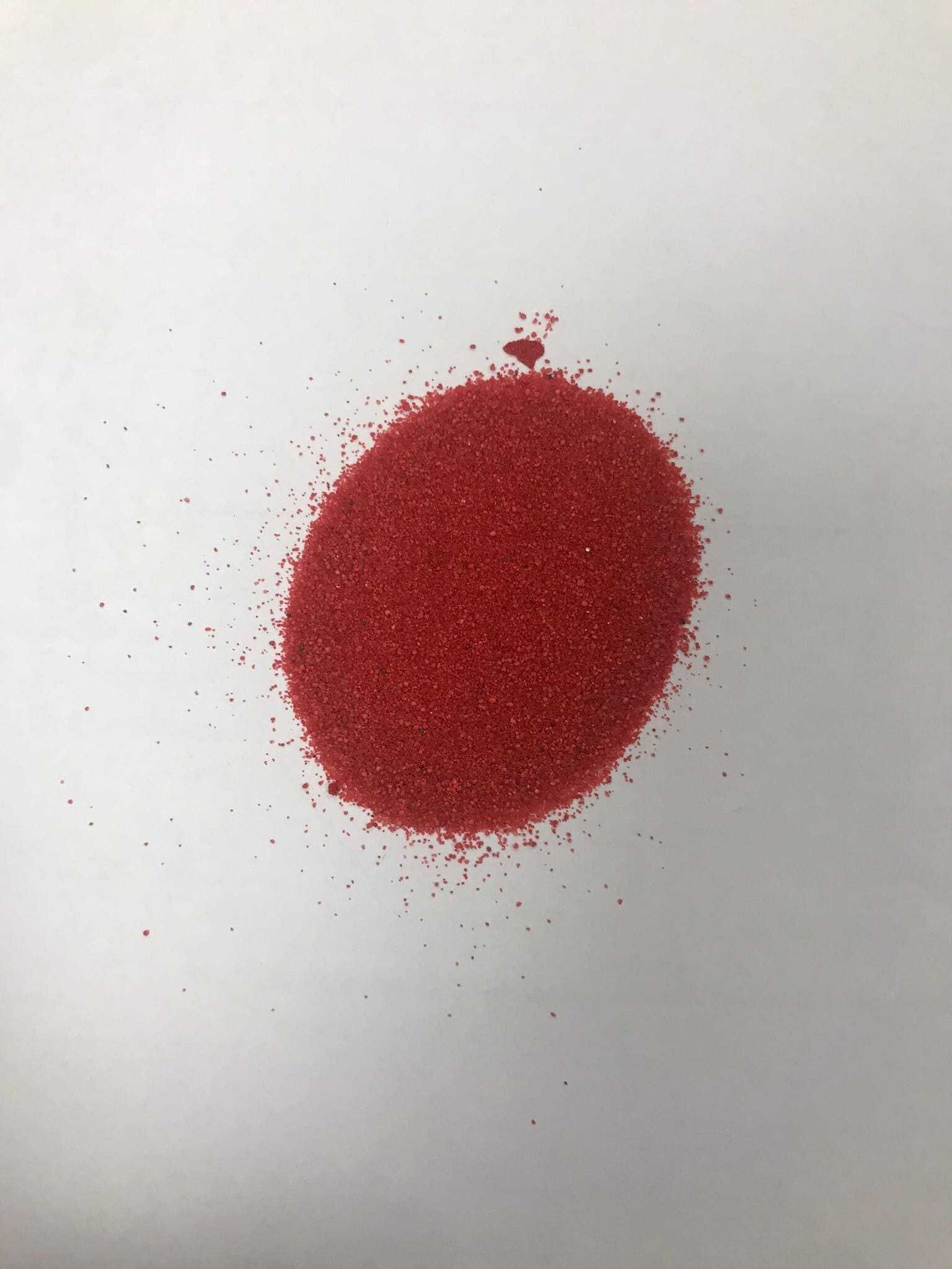 Un montón de arena roja reposa sobre una superficie blanca.