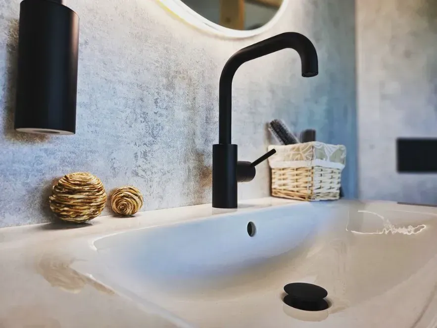 Ein Waschbecken mit schwarzem Wasserhahn und Spiegel.