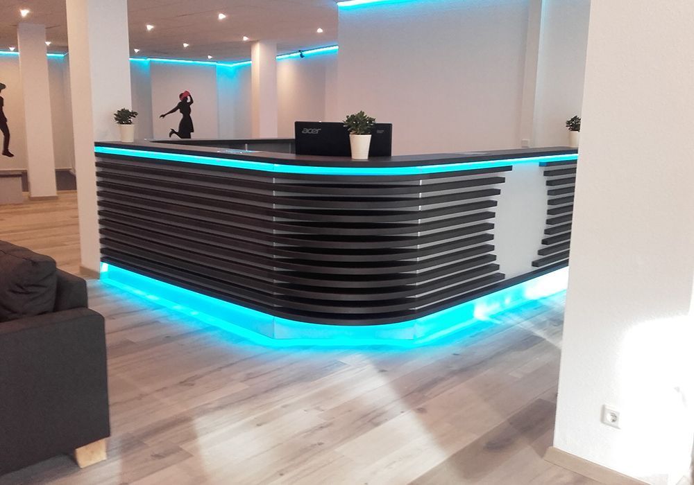 Moderne Bürolobby mit geschwungenem, schwarzem Empfangstresen, cyanfarbener LED-Beleuchtung und hellem Holzboden.