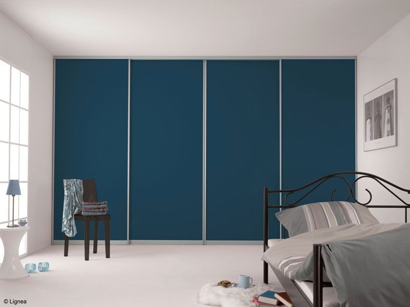 Helles Schlafzimmer mit blauen Kleiderschranktüren, weißen Wänden und einem schwarzen Metallbettgestell