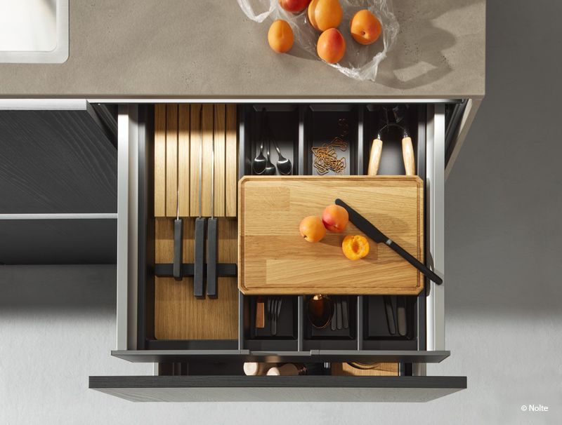 Draufsicht auf eine offene Küchenschublade mit Holzboxen, Küchenutensilien und Orangen auf der Arbeitsfläche.