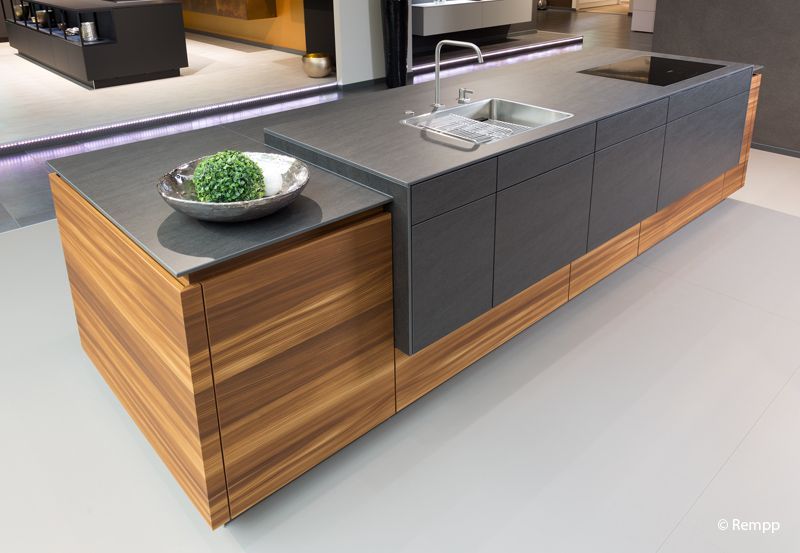 Moderne Kücheninsel mit dunkler Arbeitsplatte, Spüle und holzvertäfeltem Sockel neben einer Obstschale.