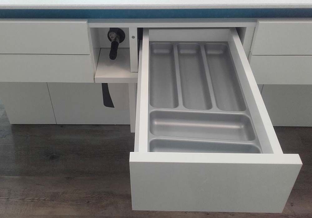 Offene Küchenschublade mit grauem Besteckkasten aus Kunststoff neben einem Schrankschloss