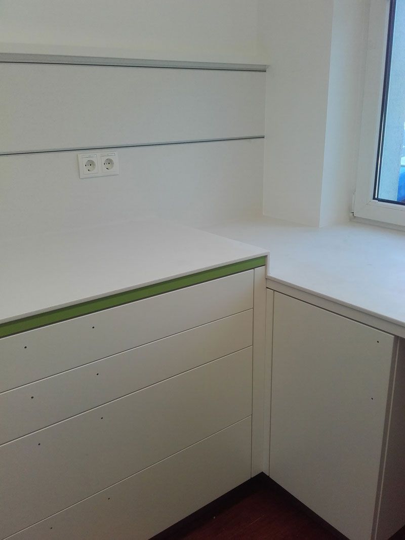 Weiße, eingebaute Schreibtischnische mit Schubladen, Regal und Fensterlicht neben einem Eckschrank.