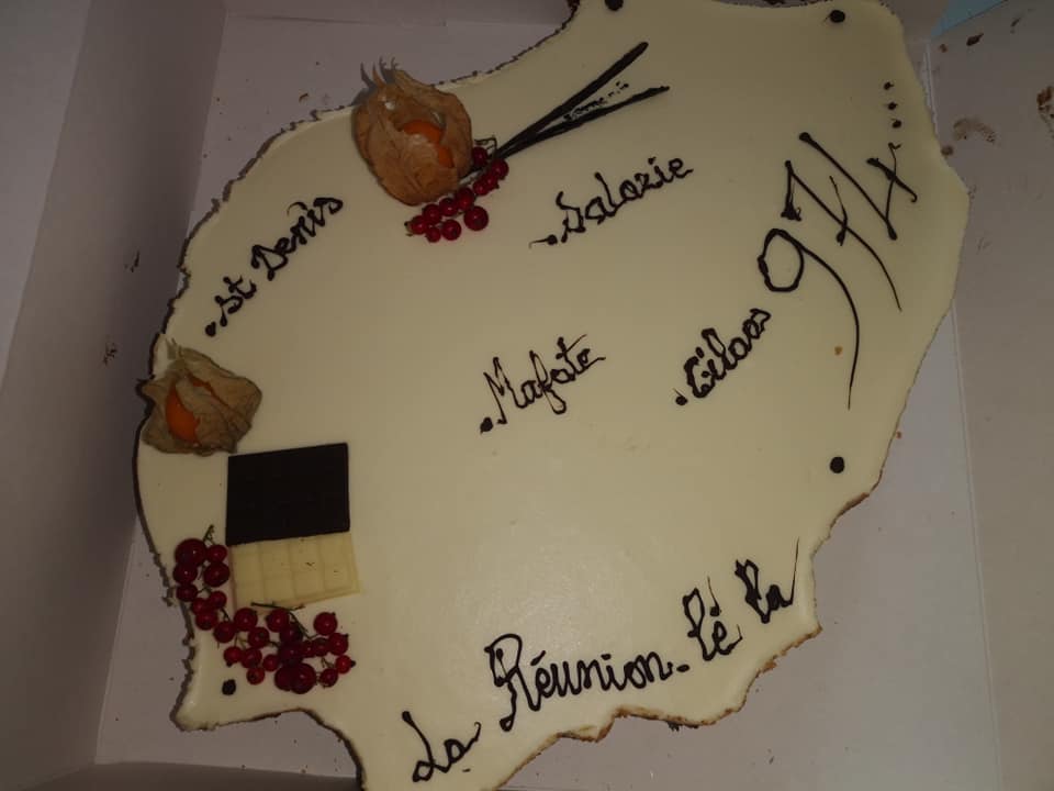 Gâteau en forme de l'île de la Réunion, décoré de texte et de fruits.