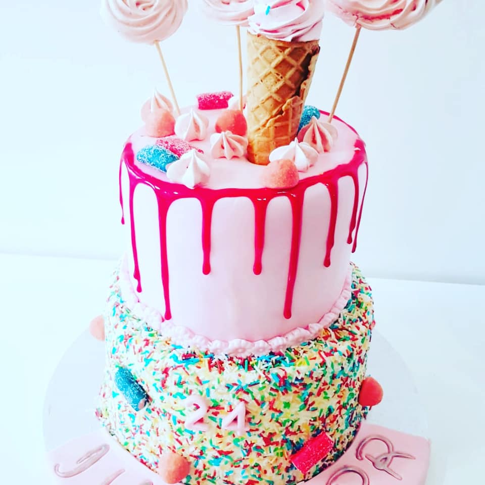 Gâteau d'anniversaire à deux étages avec glaçage rose et vermicelles, garni d'un cornet de glace, de meringues et de bonbons.