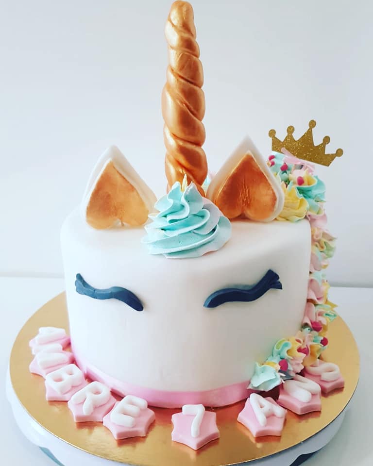 Gâteau licorne avec corne dorée, oreilles, couronne et décorations pastel.