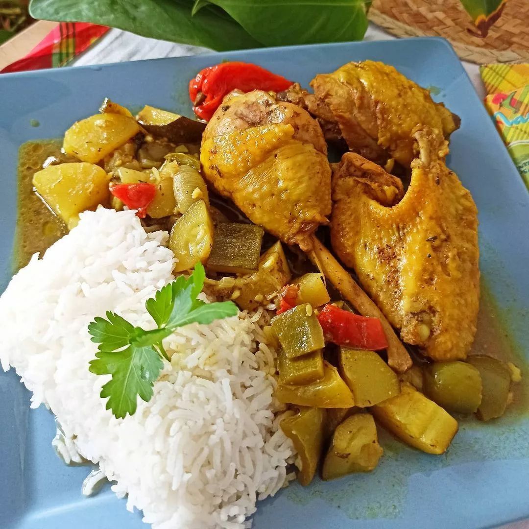Poulet au curry avec riz et légumes sur une assiette bleue.