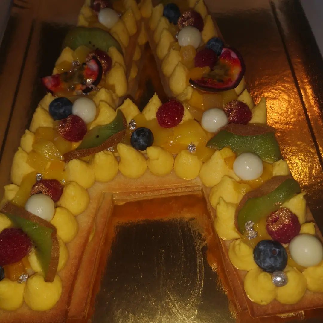 Gâteau lettre « A », décoré de glaçage jaune, de fruits et de boules de chocolat blanc.