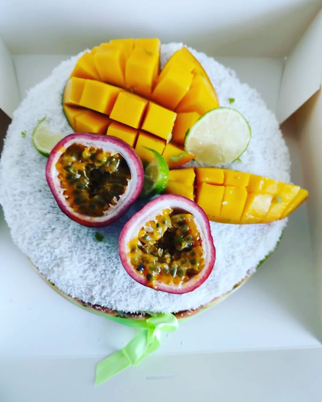 Gâteau au tapioca garni de mangue, de fruit de la passion et de citron vert dans une boîte blanche.