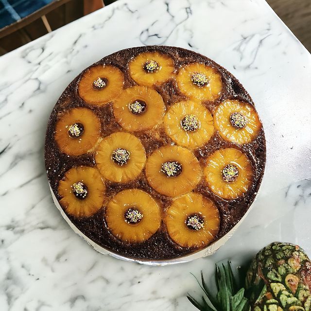 Gâteau à l'ananas renversé sur marbre, garni d'anneaux d'ananas et de vermicelles.
