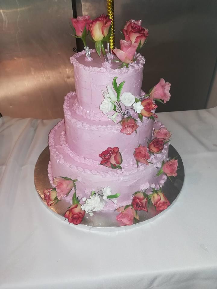 Gâteau rose à trois étages décoré de roses et de verdure, sur un plateau en argent.