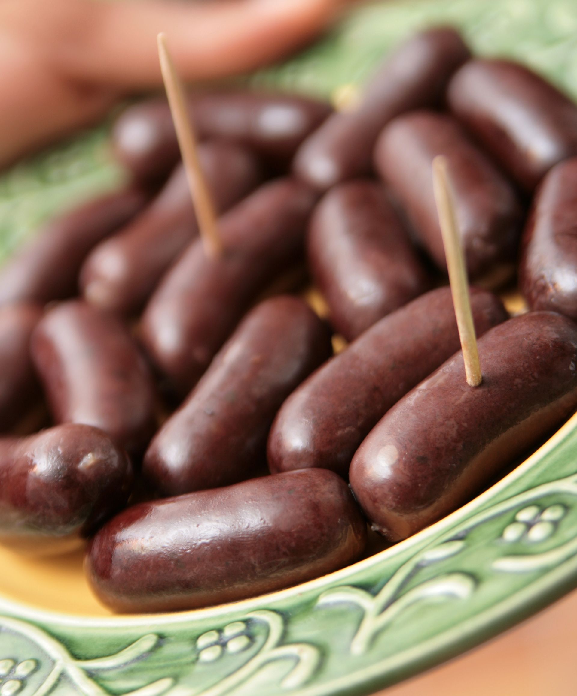 Dattes enrobées de chocolat sur une assiette verte et jaune, certaines avec des cure-dents.