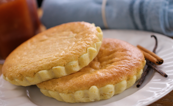 Deux tartelettes dorées sur une assiette blanche, avec des bâtons de cannelle et des gousses de vanille.