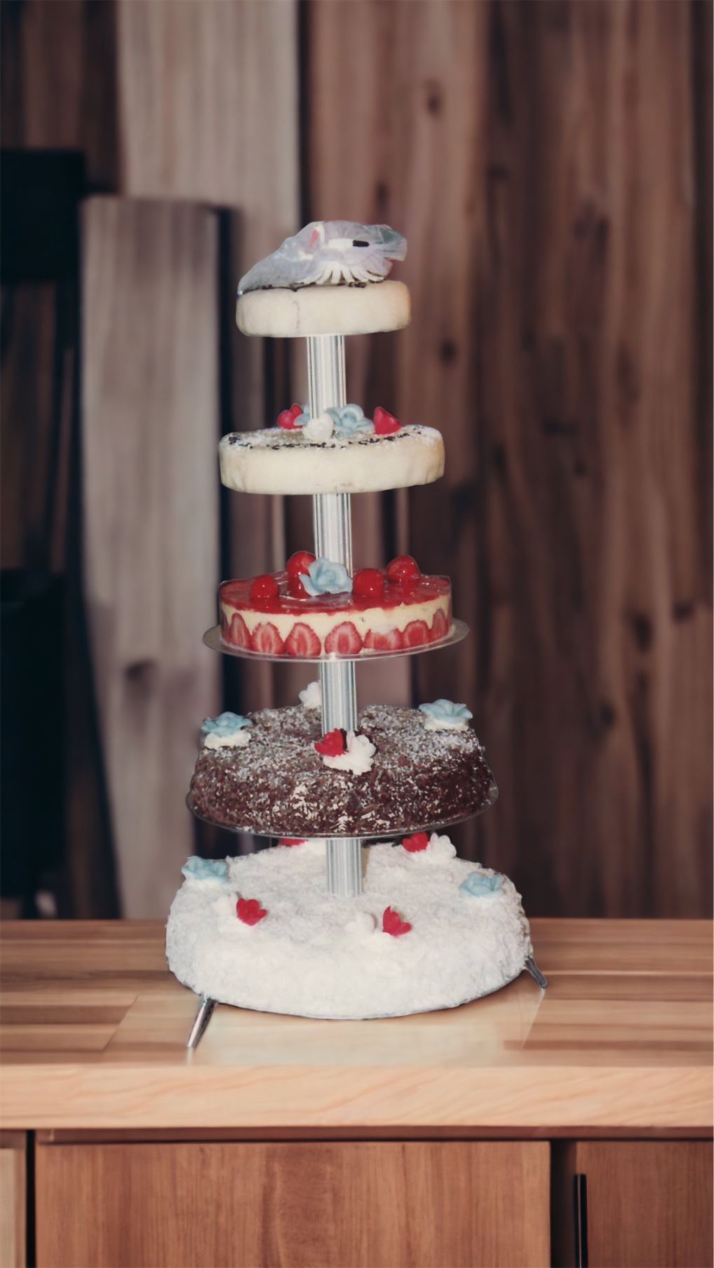 Présentoir à gâteaux à cinq niveaux avec des gâteaux décorés de fraises et de fleurs sur une table en bois.